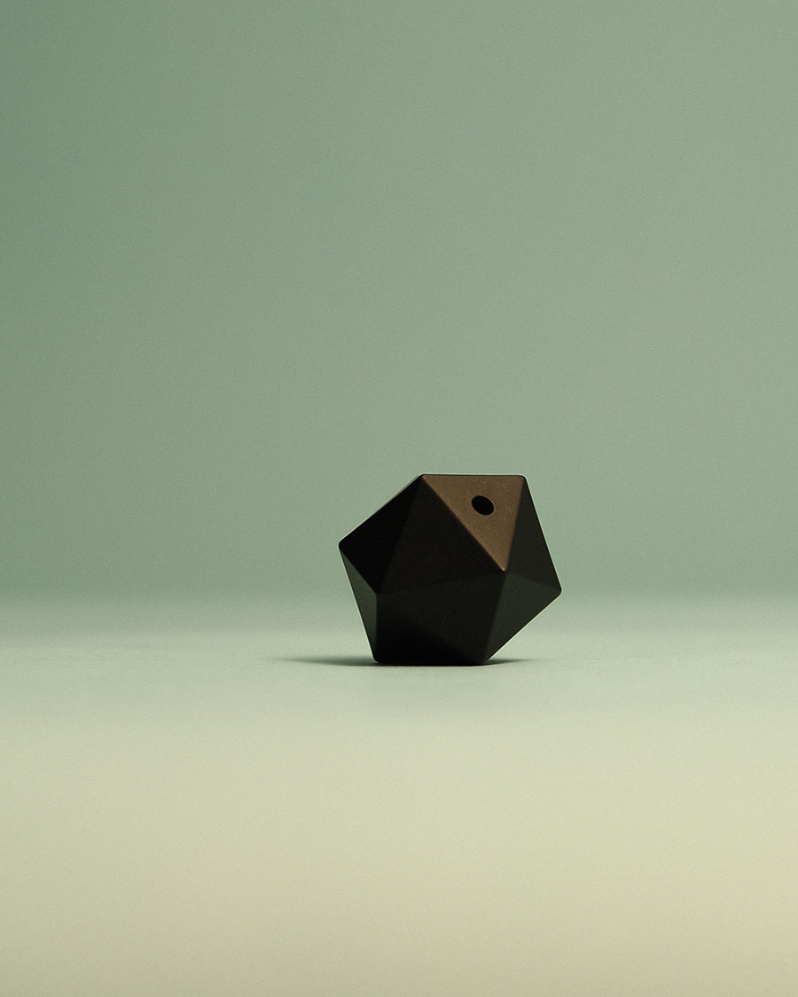 Close-up of the architectural icosahedron shape on the Hestia matte black incense stand. Black geometric object on a gradient green background