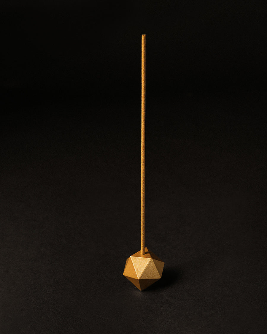 Minimalist gold incense holder resting on a tabletop, catching the light Gold geometric incense holder on a black background