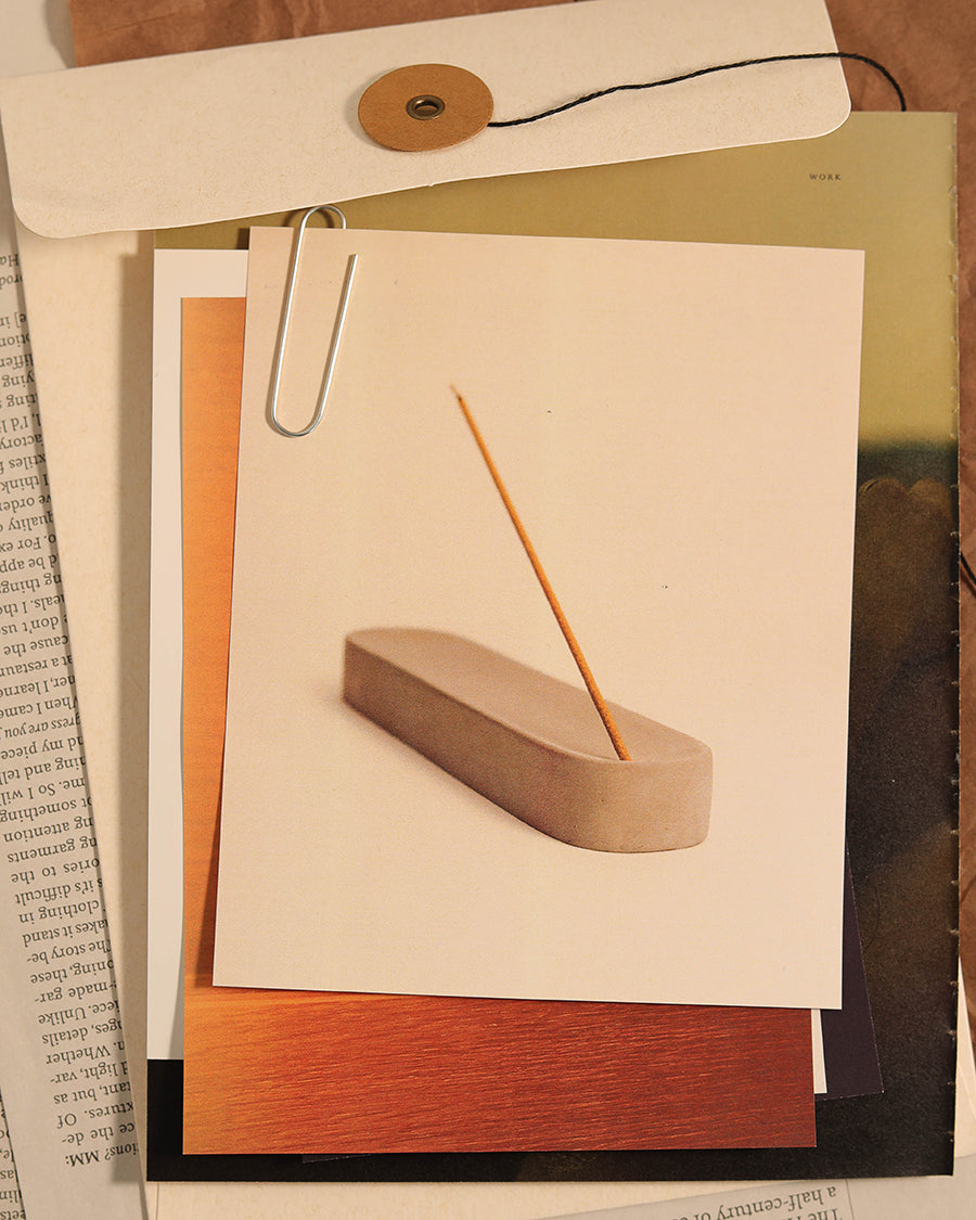 Incense holder with a single incense stick on a piece of paper, surrounded by books Modern brutalist ash catcher designed by Para Home Studio