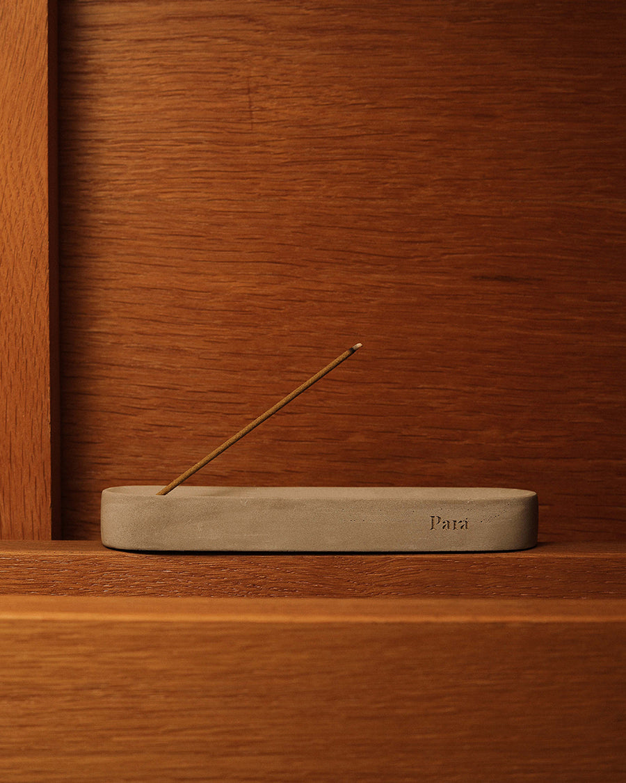 Incense stick on a concrete holder with 'Para' branding against a wooden background Tactile concrete incense holder resting on a modern tabletop.