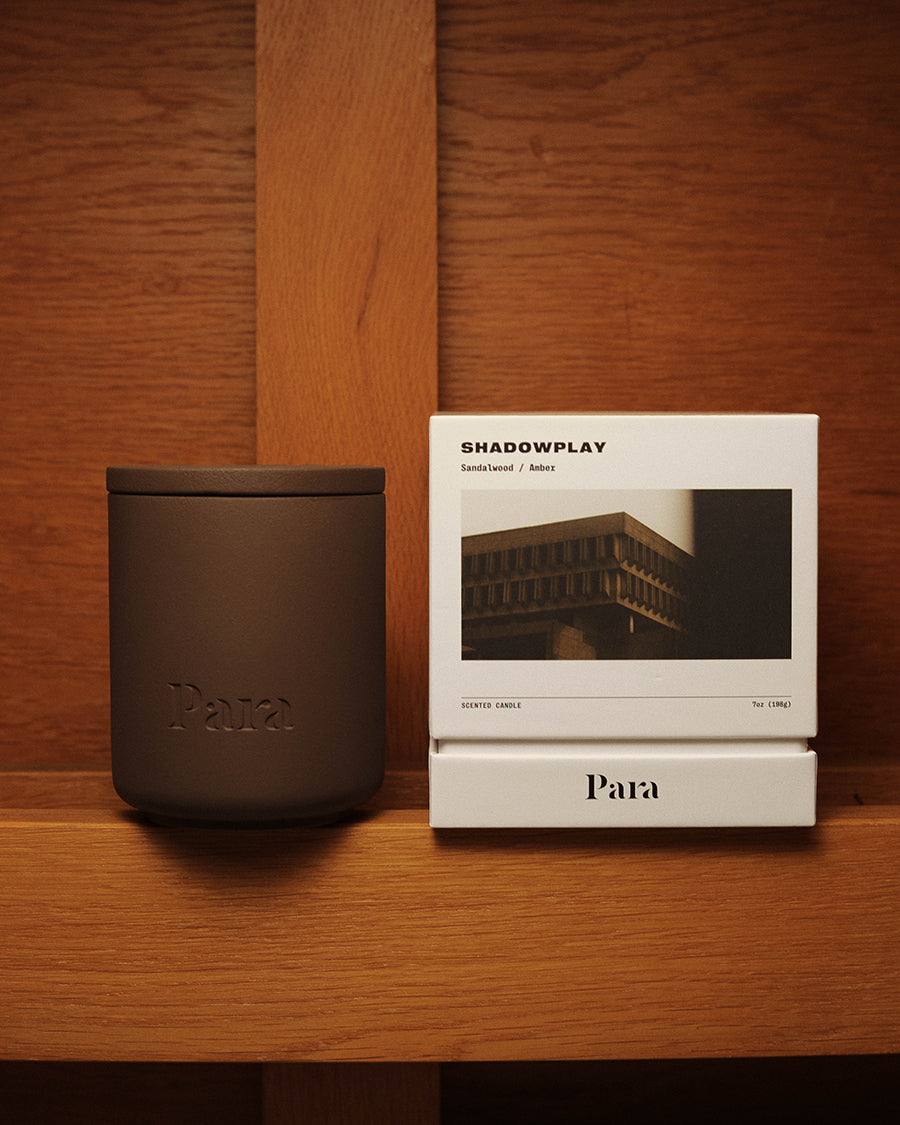 Shadowplay hand-poured sandalwood and amber candle in a brown concrete vessel by Para Home Studio Dark brown candle and white packaging with 'Shadowplay' text on a wooden surface