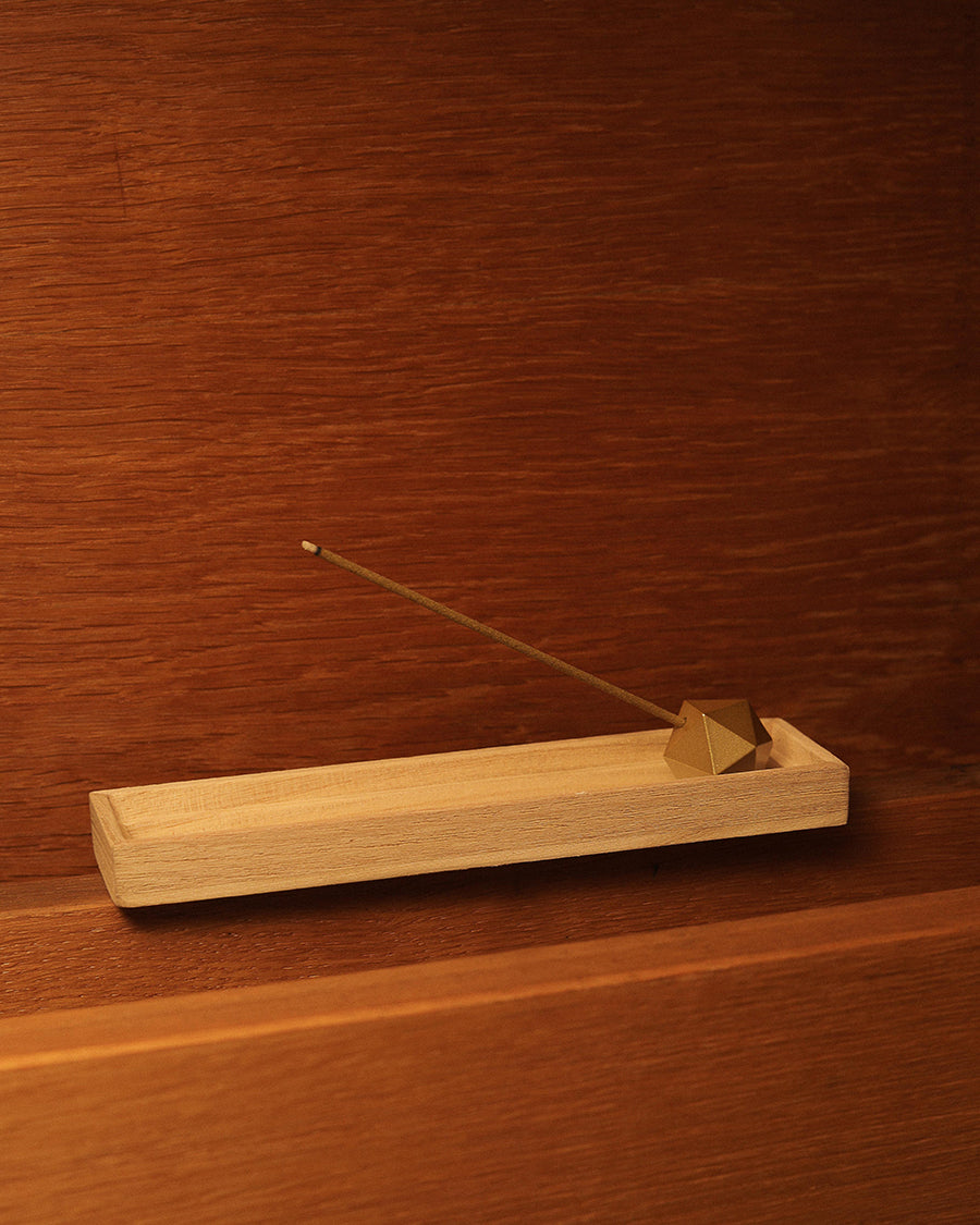 Close-up of the architectural icosahedron shape on the Hestia gold incense stand Incense burner with a single stick of incense on a wooden surface