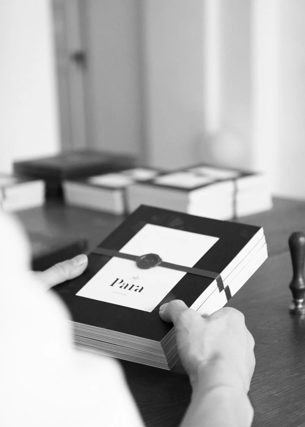 Person holding a stack of books with Para branding on a desk.