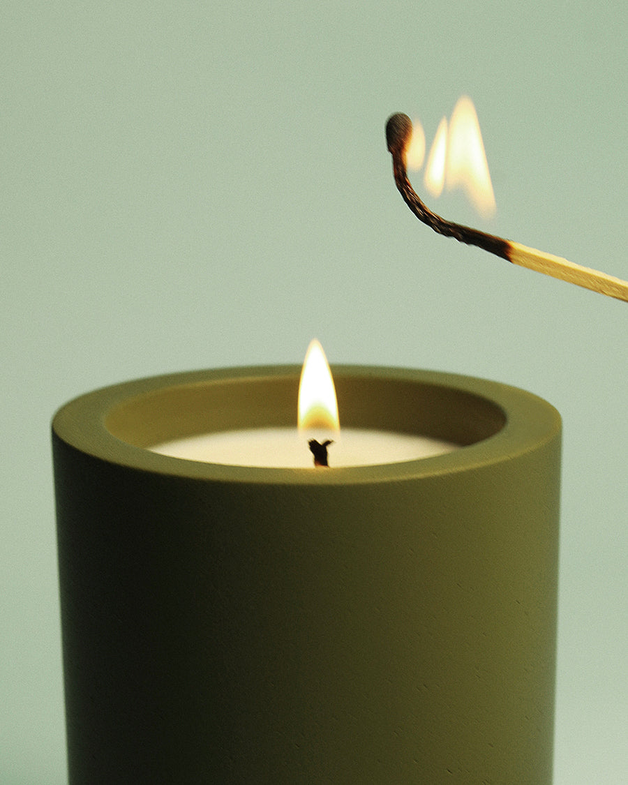 Match lighting a candle against a light green background Beyond the Pines hand-poured pine and oak moss candle in a green concrete vessel by Para Home Studio